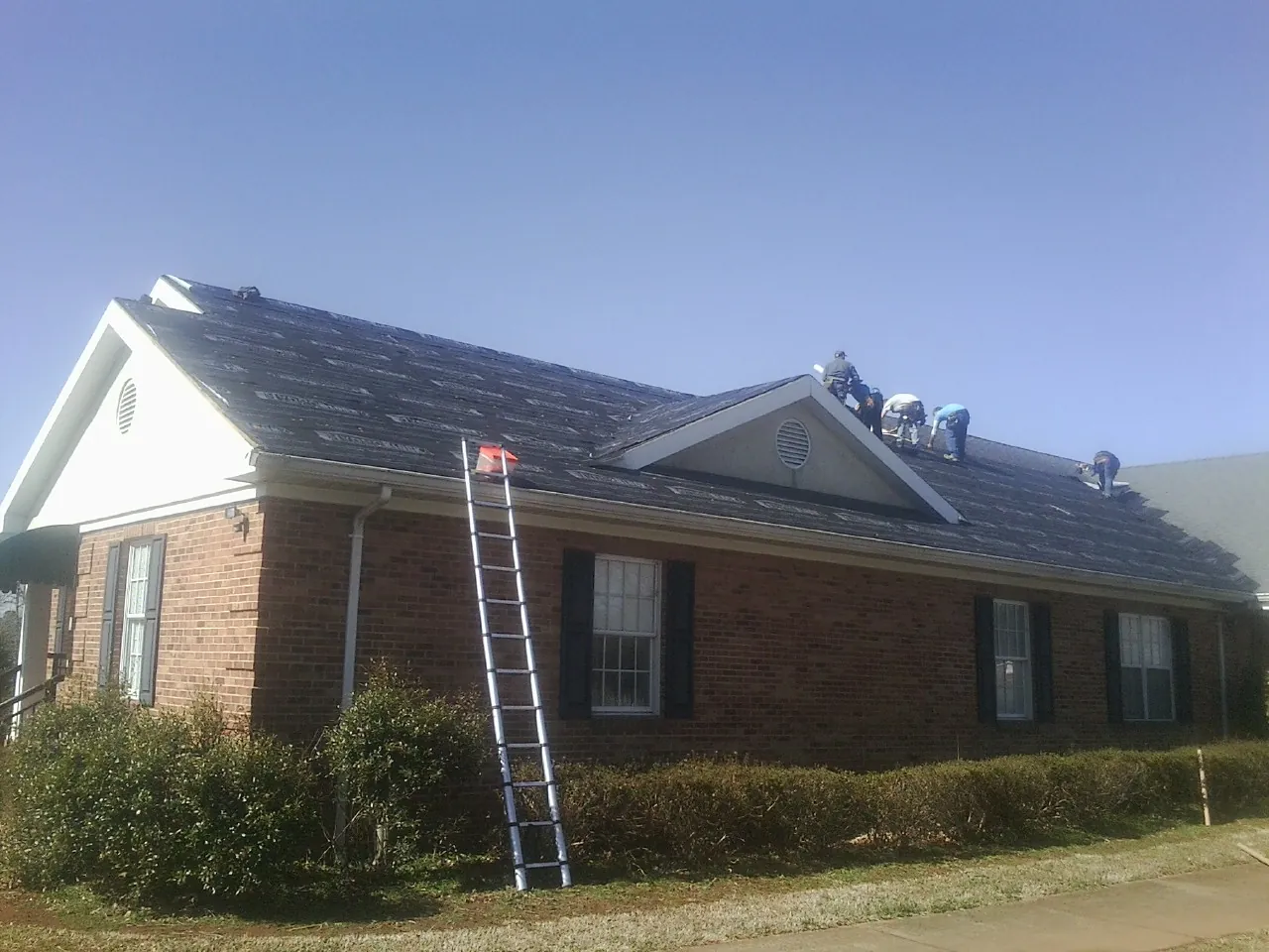 Crew tearing shingles off a brick ranch roof with a ladder set — Metal Roof Repair work by our crew in Ruffs Dale