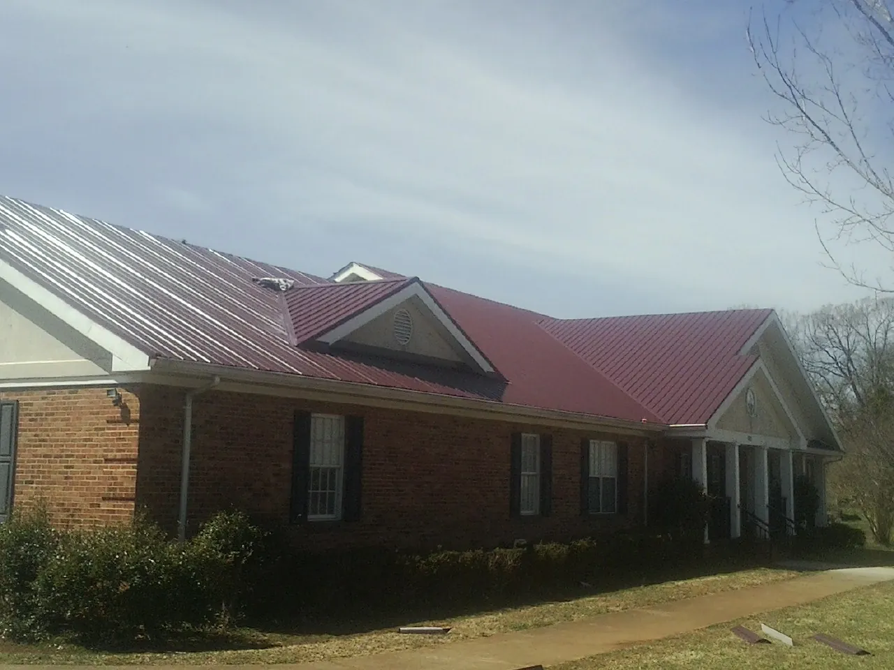 Red metal roof with gabled entries on a long brick building, from a Hail Damage Roof Repair job in Ruffs Dale