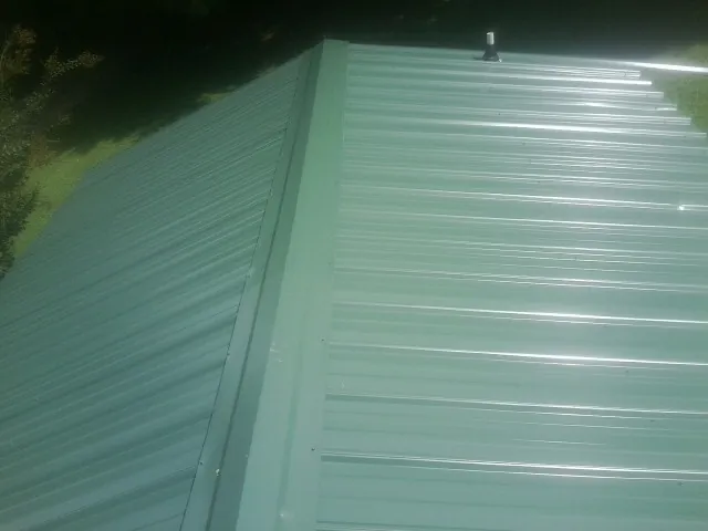 New green metal panels meeting at the ridge of a roof — Flat Roof Repair work by our crew in Ruffs Dale