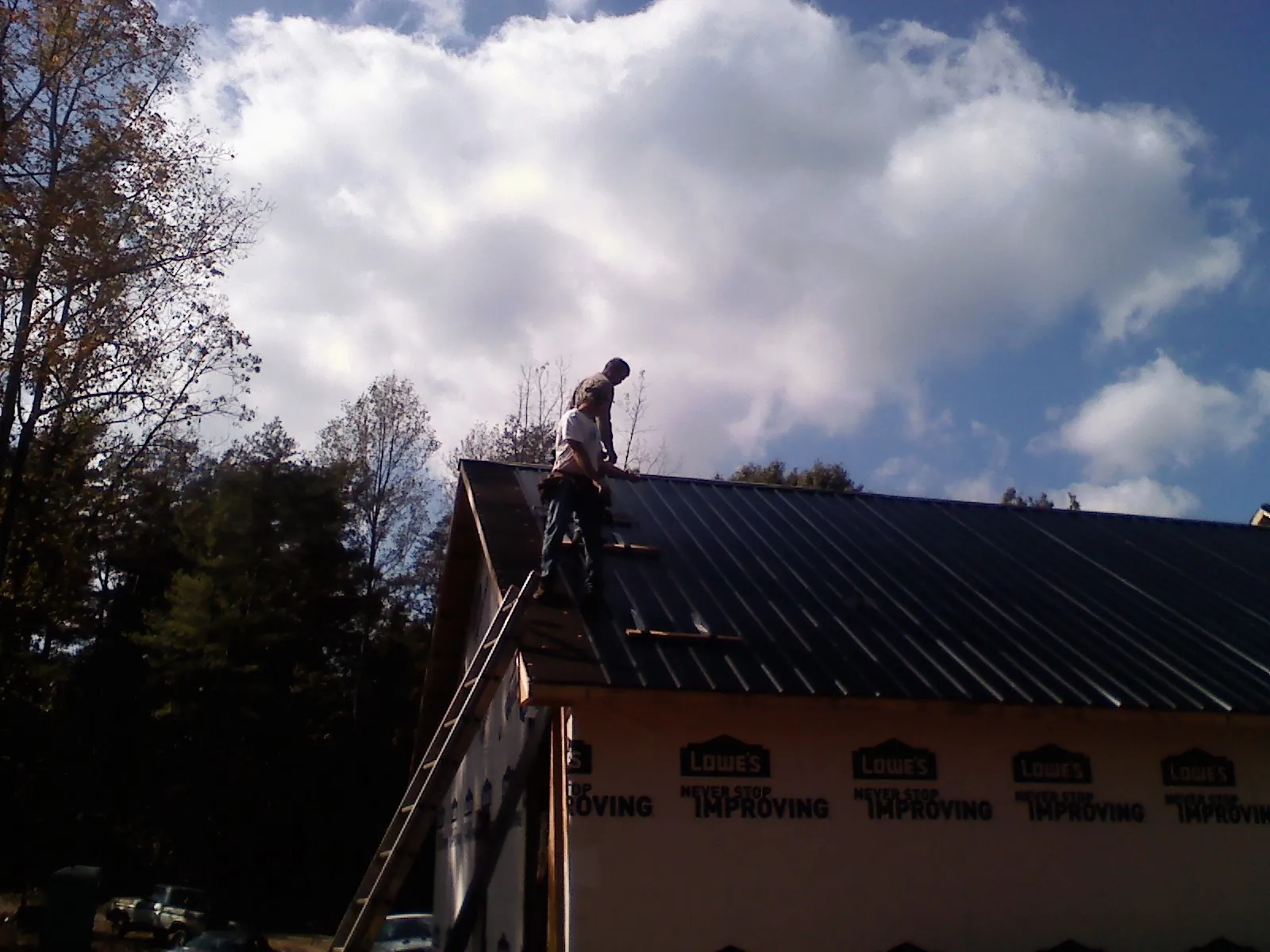 Roofer fastening dark metal panels high against a cloudy sky, from a Roof Inspection job in Ruffs Dale