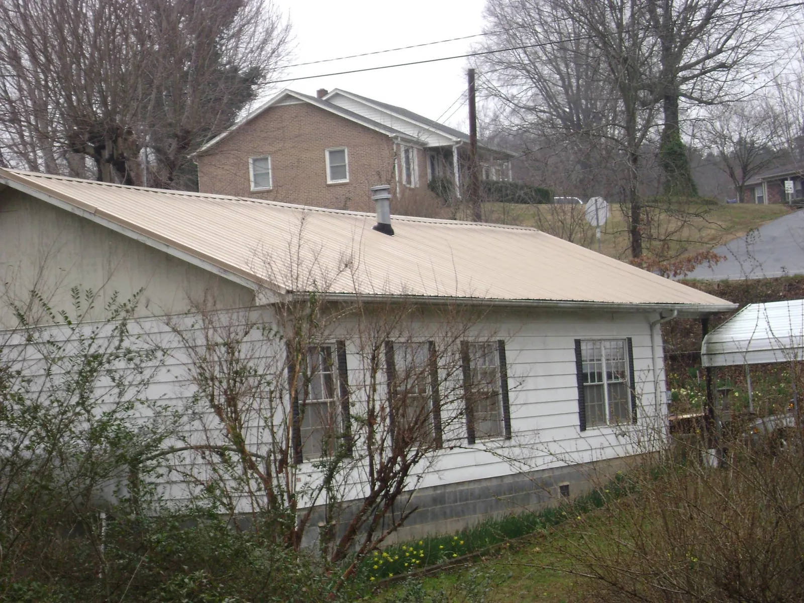 Tan metal roof on a white sided house set into a hillside — Commercial Roofing by Roofing Brothers in Ruffs Dale