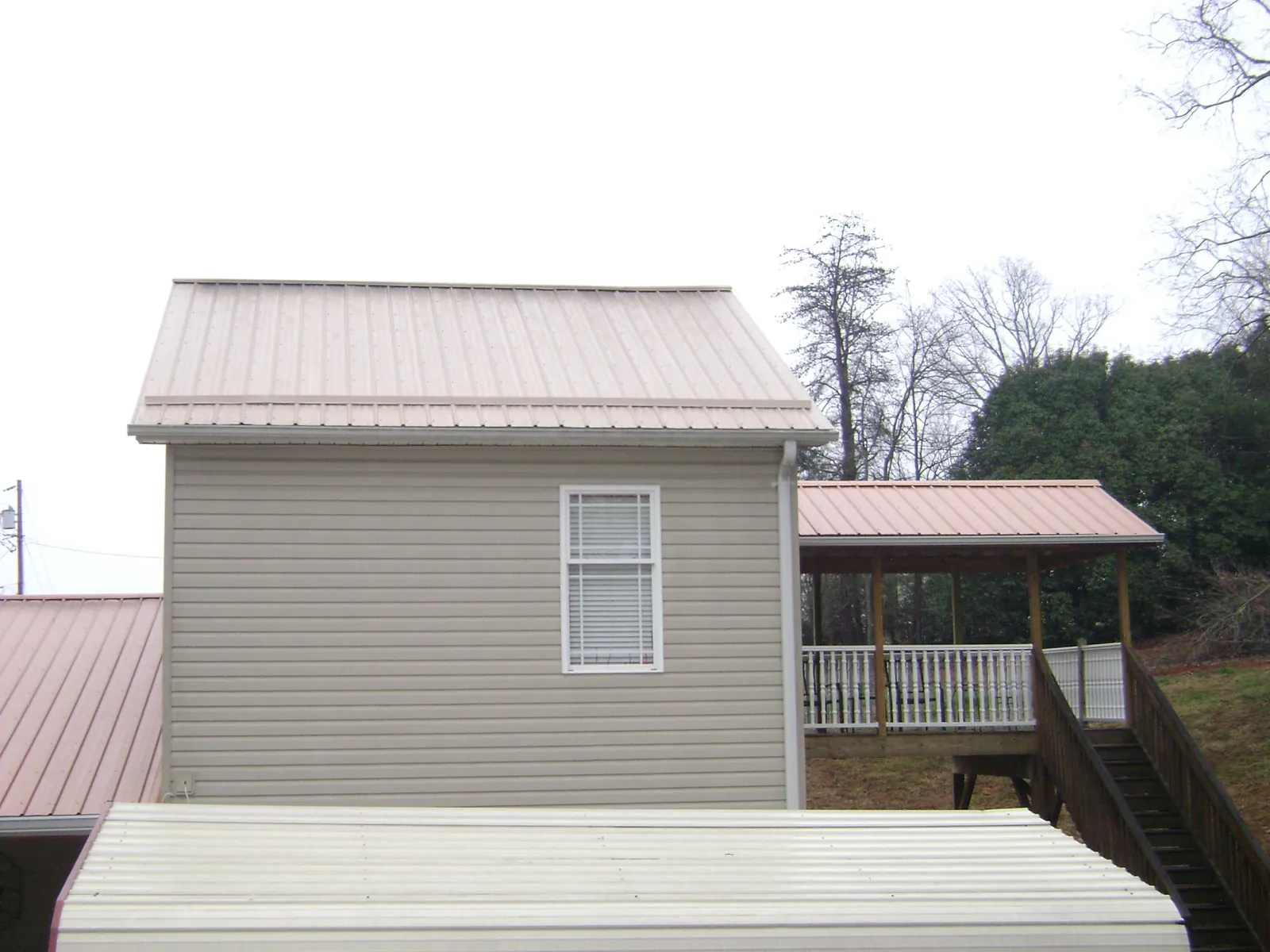 Tan metal roofs on a two story addition and attached porch, from a Roof Replacement job in Ruffs Dale