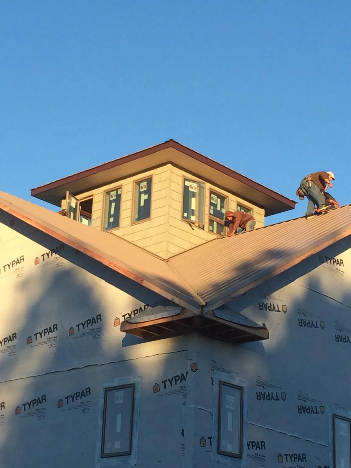 Roofers working around a rooftop cupola on a new metal roof at sunset — Roof Waterproofing in Ruffs Dale by Roofing Brothers